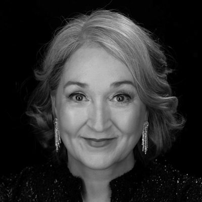 A black and white close-up of a woman with light coloured hair, wearing earrings and a dark sparkly top.