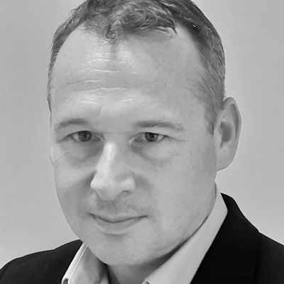 A man with short hair wearing a shirt under a suit jacket.