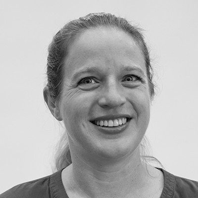 A black and white close-up of a woman with long light hair in a ponytail, smiling.