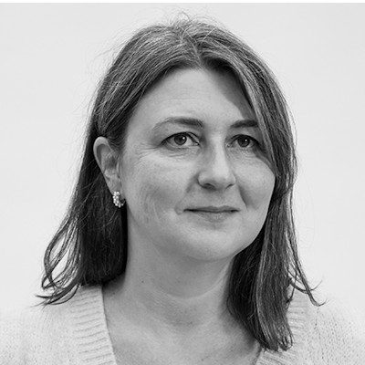 A black and white portrait of a woman with long dark hair wearing earrings and a light-coloured jumper.