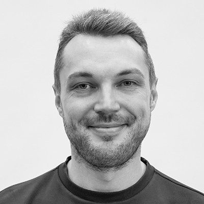 A black and white headshot of a man with short dark hair wearing a dark t-shirt.