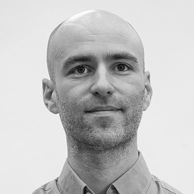 A black and white close-up of a man with a shaved head and light facial stubble.