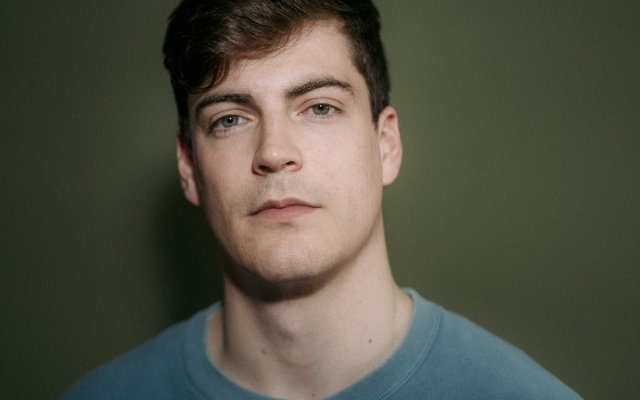 A close-up of a man with short dark hair, wearing a blue t-shirt.