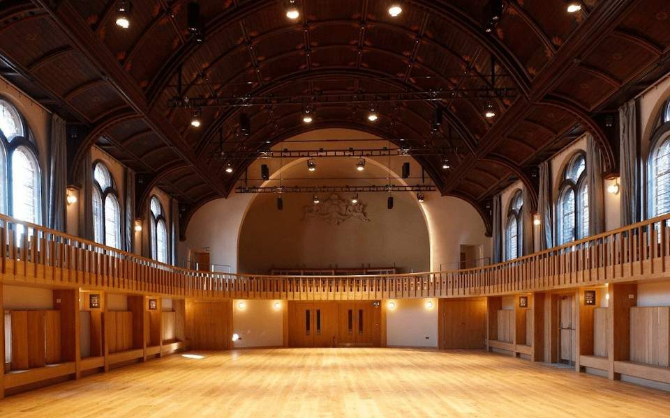 A large performance space with wooden floor and bay windows along each side.