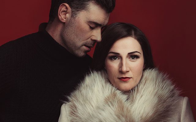 A man wearing dark clothes holding a woman in a light fur coat.