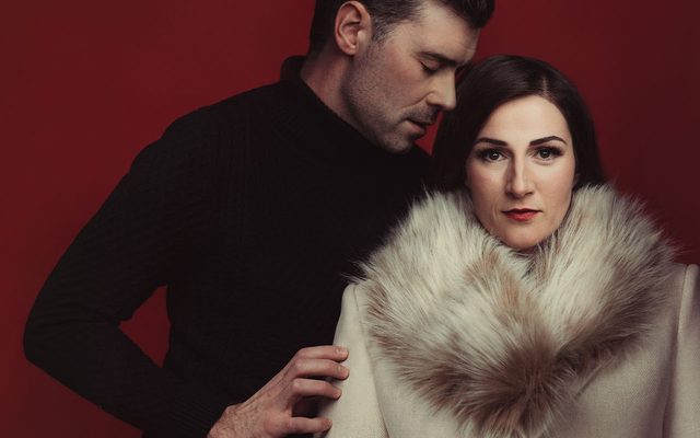 A man wearing dark clothes holding a woman in a light fur coat.