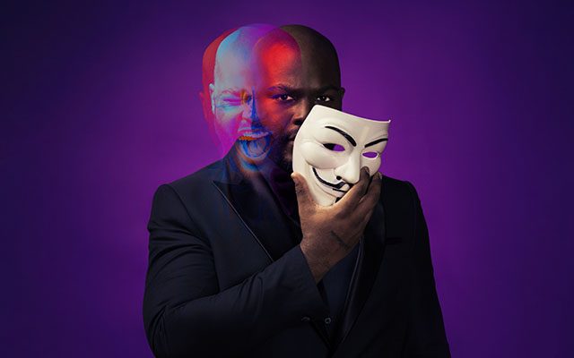 A ghostly, blurred image of a man holding a mask to his face with two expressions:one of anger and one smiling.