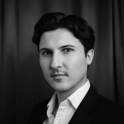 A black and white portrait of a man wearing a white shirt and dark jacket, with short dark hair.