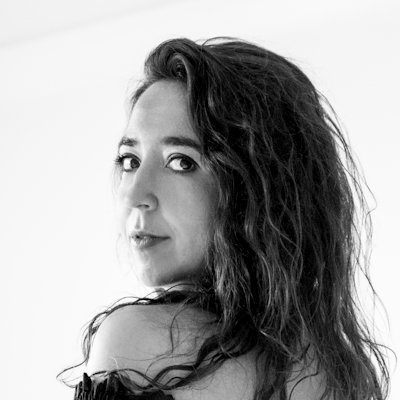 A black and white portrait of a woman with long dark hair looking over her shoulder.