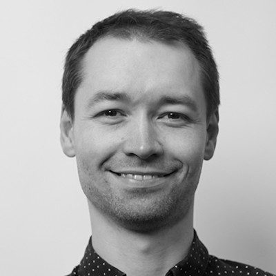 A black and white close-up of a man with short dark hair smiling.