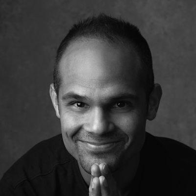 A black and white portrait of a man with short dark hair smiling.