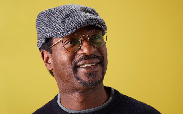 An image of Chris Dawkins wearing a flat cap and glasses, smiling.