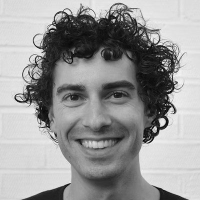 A close-up of a man with medium length, dark curly hair smiling.