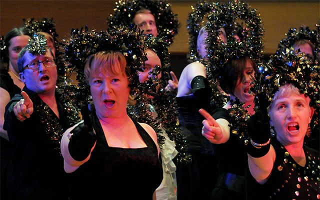 A group of people singing and dancing, with tinsel on their heads and hair.