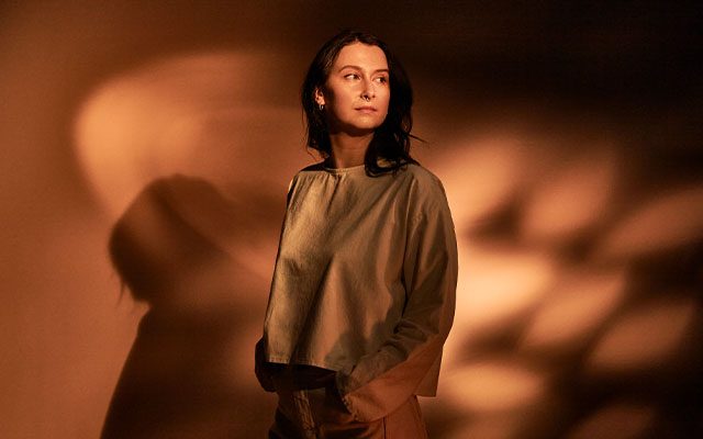 A woman with long dark hair wearing a gold coloured top.