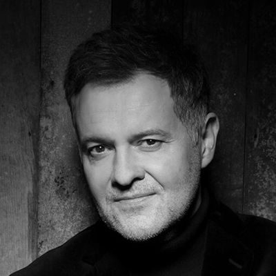 A black and white portrait of a man with short dark hair, wearing a dark jumper.