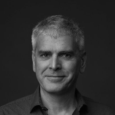 A black and white portrait of a man with short light hair smiling.