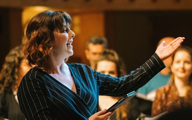A woman singing with her arm outstretched to a small group during an Opera North Sing ON event.