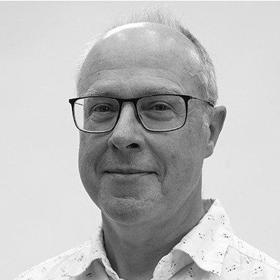 A black and white portrait of a bald man wearing glasses and a white shirt.
