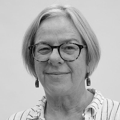 A black and white portrait of a woman with medium-length light hair, wearing dark glasses and a light striped shirt.