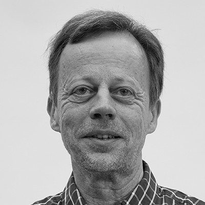 A black and white close-up of a man with short dark hair wearing a tartan pattern shirt.