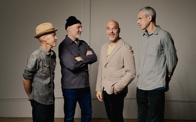 Four men; the members of The Bad Plus, standing together in an indoor setting.