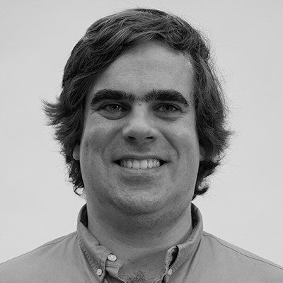 A black and white close-up of a man with medium-length dark hair, smiling.
