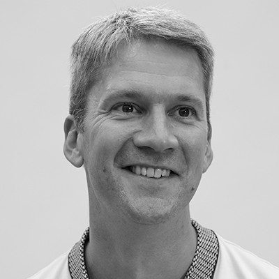 A black and white close-up of a man with short blonde hair wearing a light-coloured jumper.