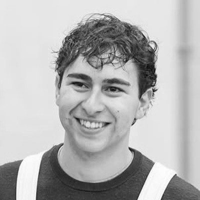 A black and white close-up of a man with short, dark curly hair smiling.
