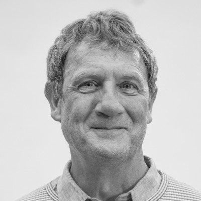 A black and white close-up of a man with short light-coloured hair wearing a light-coloured shirt.