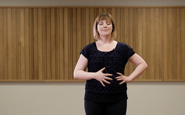 A woman standing with her eyes closed and one hand on her diaphragm as part of a Howard Opera Centre singing and breathing workshop.