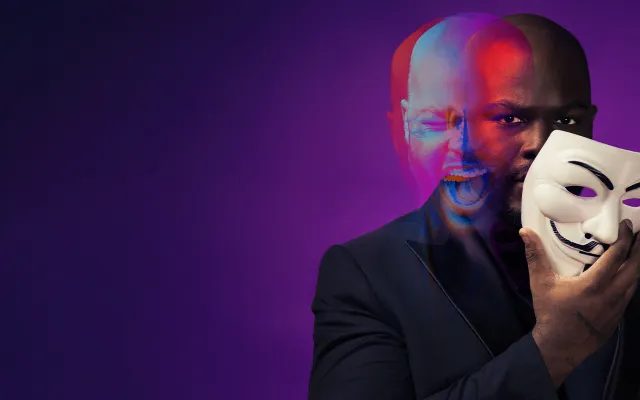 A ghostly, blurred image of a man holding a mask to his face with two expressions:one of anger and one smiling.