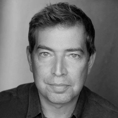A black and white close-up of a clean-shaven man with short dark hair, wearing a dark shirt.