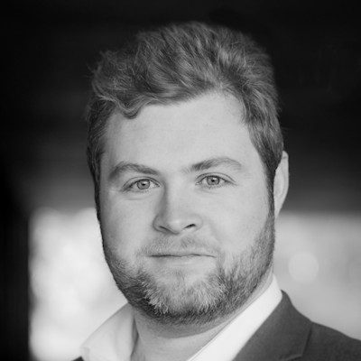 A black and white close-up of a man with short dark hair wearing a suit.