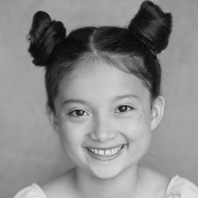 A black and white headshot of a smiling young girl with her dark hair styled in two space buns.