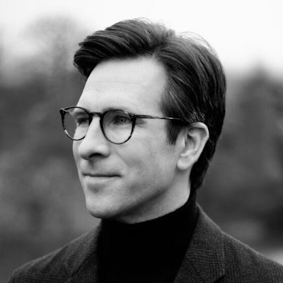 A black and white close-up of a man wearing dark clothes and glasses.