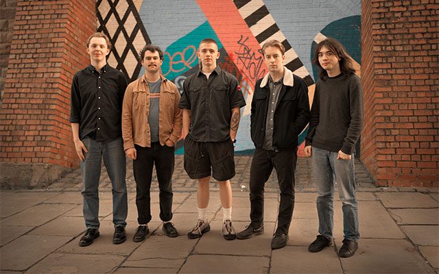 The Jack Pearce Quintet; Five individuals standing in front of a graffiti-sprayed wall.
