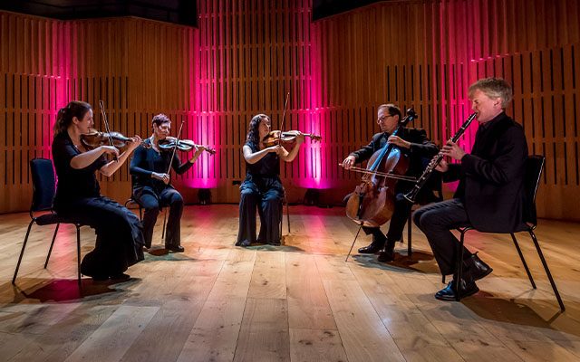 A five-piece chamber ensemble performing on stage, featuring a clarinettist, a cellist, a violist, and two violinists.