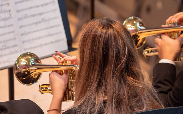 A close-up of people playing trumpets in front of sheet music.
