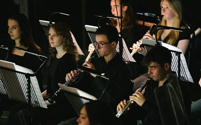 A large wind section of an orchestra, playing assorted wind instruments.