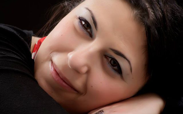 A close-up of a woman with dark hair leaning on her hand.