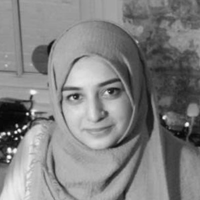 A black and white portrait of Khadija Raza wearing a hijab, smiling gently.
