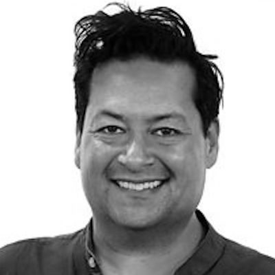A black and white close-up of a man with short dark hair, smiling.
