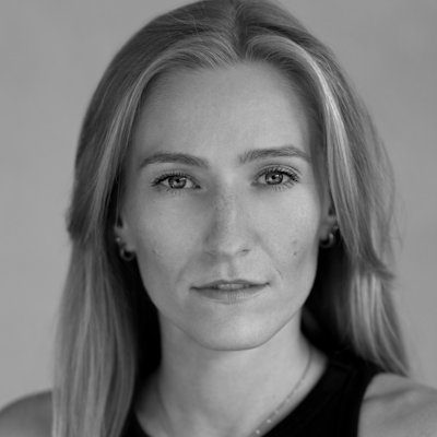 A black and white close-up of a woman with long blonde hair wearing a dark top and necklace.