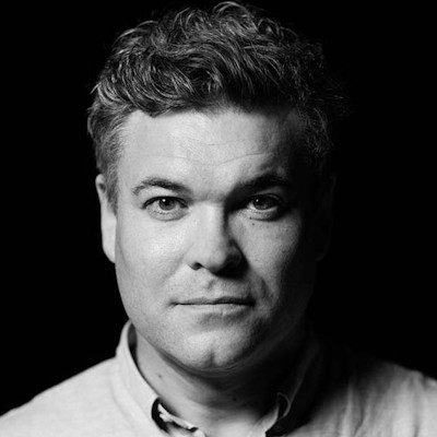 A black and white headshot of a man with short dark hair, wearing a light coloured shirt.