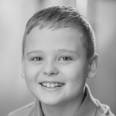 A black and white headshot of a boy with short blonde hair wearing a light shirt.