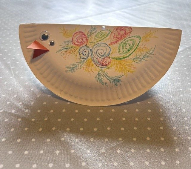 A paper plate with googly eyes, a beak and colourful swirls drawn on its side.