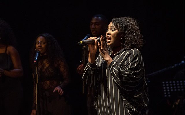 A woman singing into a microphone, in front of a group of other singers.