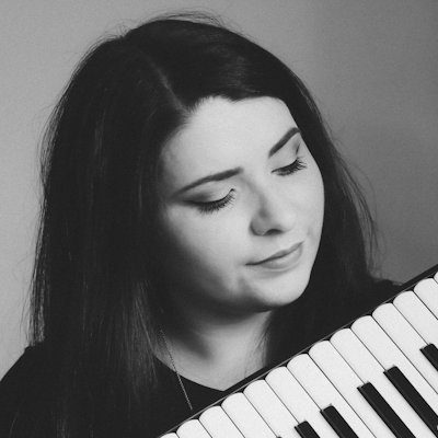 A black and white close-up of a woman with long dark hair, playing an accordion.