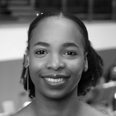 A black and white close-up of a woman with her hair tied back, smiling.